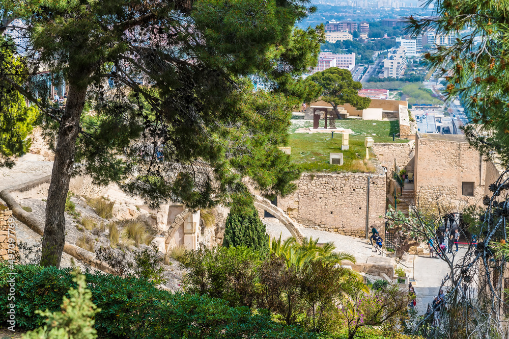 A view framed by trees across the summit of the castle of Saint Ferran above Alicante on a spring day
