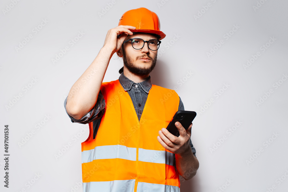 Young construction worker with smartphone in hand on white background.