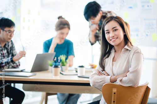 A positive secretary smiles for the camera during a meeting with colleagues working in the background.