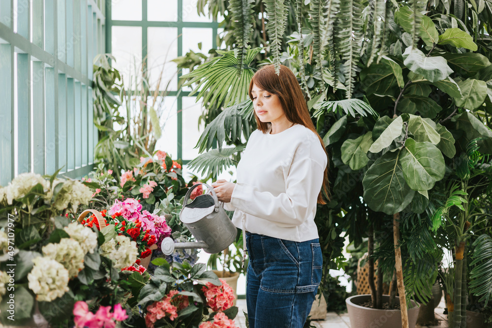 young woman plus size model waters flowers from watering can in greenhouse with tropical plants and potted plants, spring concept of urban and home jungles, place for rest and relaxation mental health young woman plus size model waters flowers from watering can in greenhouse with tropical plants and potted plants, spring concept of urban and home jungles, place for rest and relaxation mental health