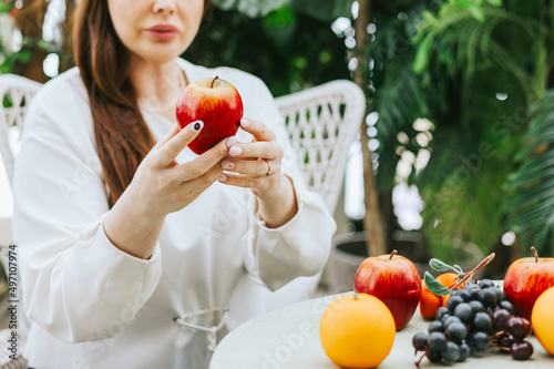 young woman plus size model sitting with apple in hands in greenhouse with tropical plants and potted plants, spring concept of urban and home jungles, place for rest and relaxation and mental health