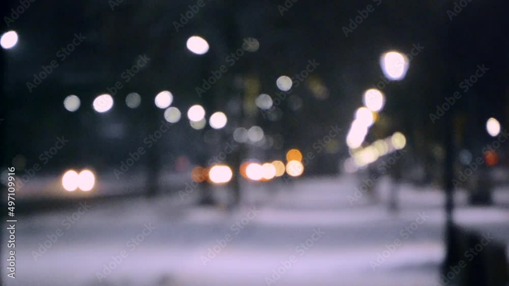 Blurred background. City view, lights, falling snow, night, street, bokeh spots of headlights of moving cars. Diffuse Urban backdrop winter scenery of street in city at night. Lantern light, snowfall