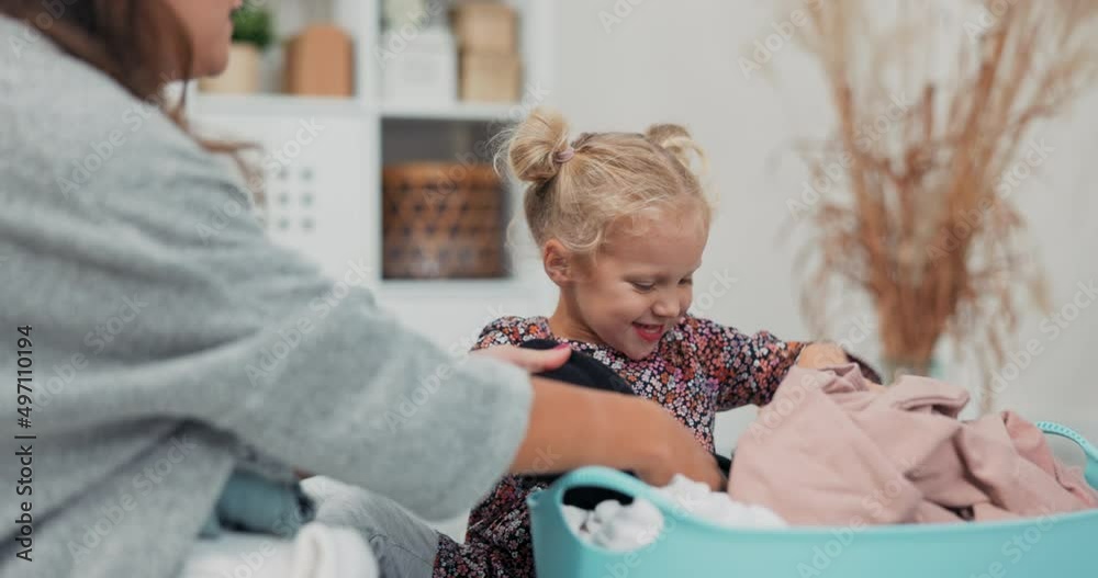 A woman and little daughter with blonde hair and blue eyes fold clean laundry taken from the clothes dryer, the little girl pulls out a sweatshirt and hands it to her mother, they watch. A woman and little daughter with blonde hair and blue eyes fold clean laundry taken from the clothes dryer, the little girl pulls out a sweatshirt and hands it to her mother, they watch.