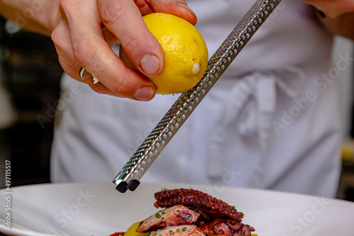 The cook grates the lemon zest to prepare the dish photo