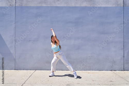 woman dancing with leg extended in front of gray blue wall 