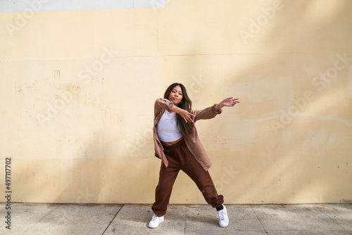 Woman dancing in front of beige wall wide stance with arms to side