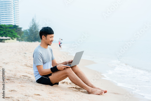 A handsome Asian man sits at the beach explaining his work to his supervisor, via video call on his laptop computer, comfortably at the beach,work from home.