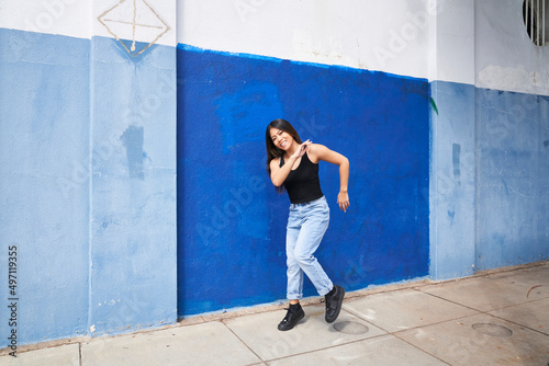 Woman dancing in front of blue wall outdoors with hand touching shoulder
