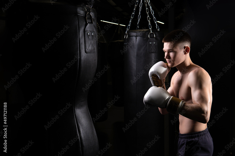 Blows practices athlete the bag boxer The glove black young male boxing, from strength fighter from punch from fit guy, studio martial. Person active dark, fitness
