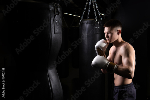 Blows practices athlete the bag boxer The glove black young male boxing, from strength fighter from punch from fit guy, studio martial. Person active dark, fitness