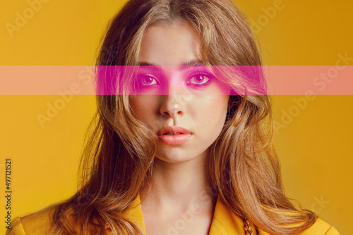 The girl, like a doll, stands straight on a yellow background with pink eyes. Stylish appearance. Close-up of a handsome teenager. The concept of naivety and youthful maximalism