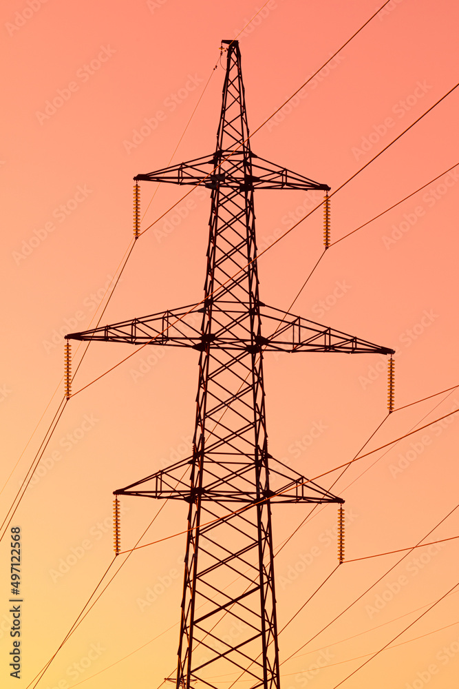 Background, view or scene of steel tower of electric main or electricity transmission line with the wires silhouette on yellow, orange and red background of sunset or sunrise sky Background, view or scene of steel tower of electric main or electricity transmission line with the wires silhouette on yellow, orange and red background of sunset or sunrise sky