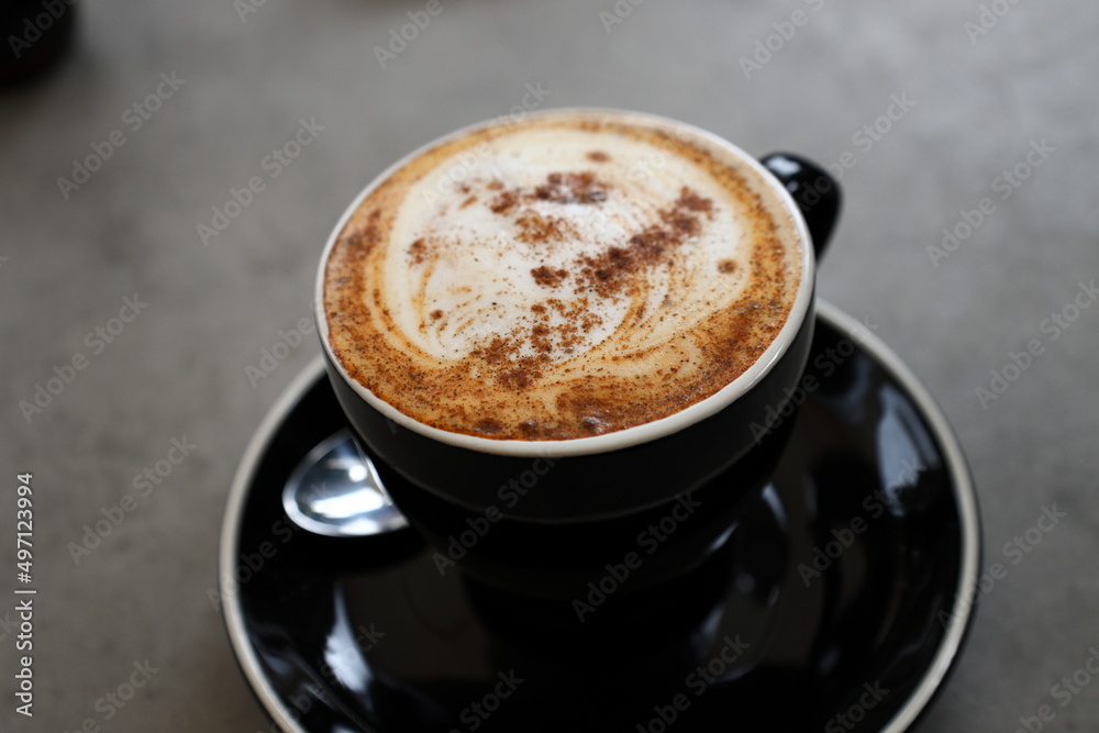 A close-up photo of a cup of cappuccino presented in a black cup. A close-up photo of a cup of cappuccino presented in a black cup.