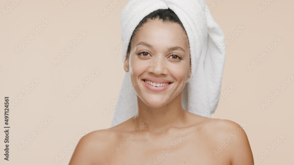 Beauty portrait of young cheerful African American woman with a towel on her head and naked shoulders who smiles wide for the camera on beige background | Skin and body care concept Beauty portrait of young cheerful African American woman with a towel on her head and naked shoulders who smiles wide for the camera on beige background | Skin and body care concept