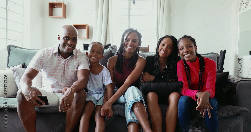 Family posing for photo at home couch, black African ethnicity parents and children smiling at camera Family posing for photo at home couch, black African ethnicity parents and children smiling at camera