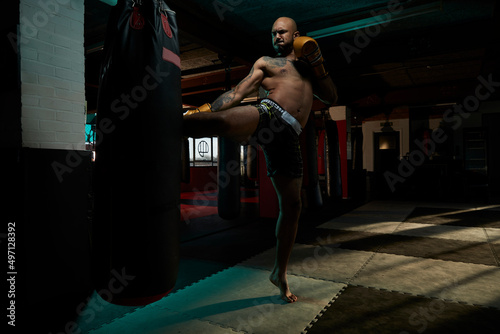 Shirtless boxer kicking punching bag in gym photo