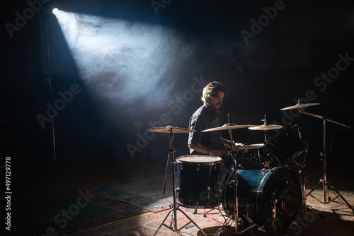 Photo Young drummer sitting in spotlight and training in hall