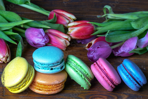 French macaroni on the background of a beautiful bouquet of flowers lie on a wooden background. Close-up. photo