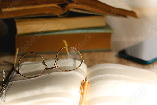 Open book, mechanical pencil, reading glasses, mobile phone and strack of books on the desk. Studying concept. Selective focus.