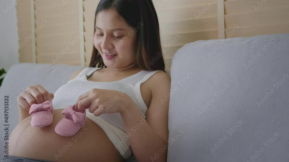 Young pregnant woman putting baby shoes on tummy, family and pregnancy care concept