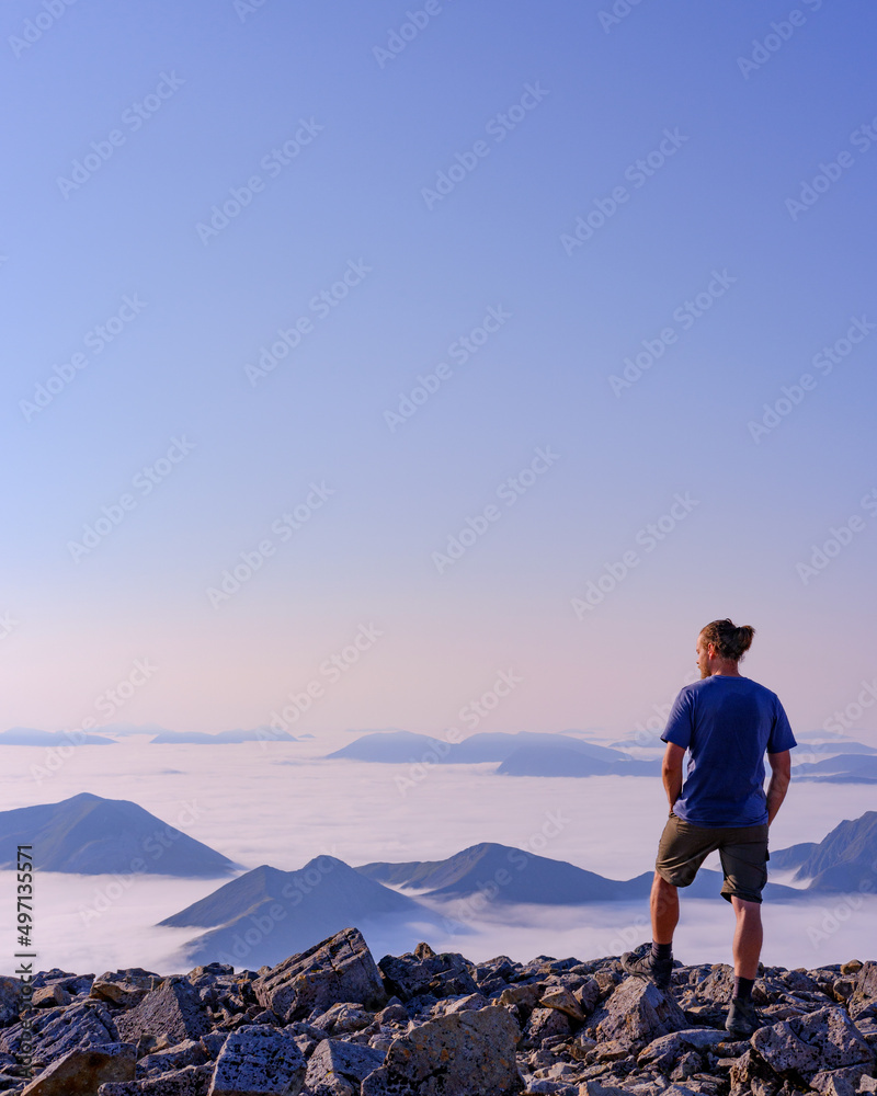 man stood at the summit of a mountain above the clouds after hike