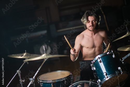 Excited young rock drummer playing drum set in studio. Man with moustache sitting shirtless at drum set and rehearsing or recording music. Drummer training concept