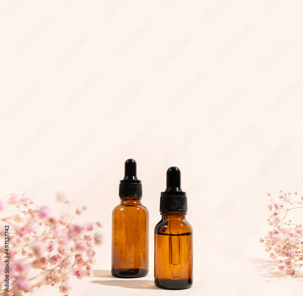 Brown glass cosmetic bottles with pipette, dry pink flowers on beige background with sun shadows. Natural organic cosmetics for face and body, aroma oil. Beauty concept. Products for branding, mock up Brown glass cosmetic bottles with pipette, dry pink flowers on beige background with sun shadows. Natural organic cosmetics for face and body, aroma oil. Beauty concept. Products for branding, mock up