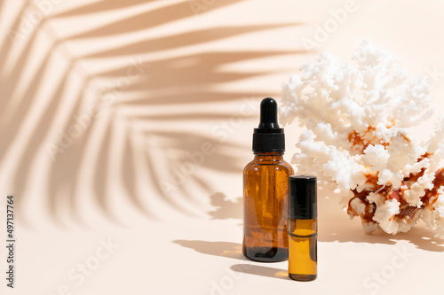 Brown glass cosmetic bottles with pipette  sea coral  sun shade tropical leaf on beige background. Natural cosmetics for face and body  aroma oil. Beauty summer concept. Products for branding  mock up