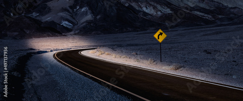 Desert highway at night illuminated by the glow of car headlights with a right curve road sign