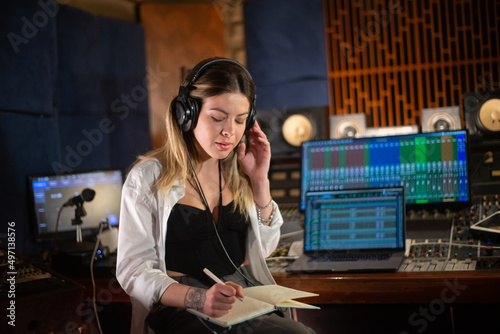 Female music producer listening to music and taking notes in notepad. Young Caucasian woman working in sound recording studio. Creating music concept photo