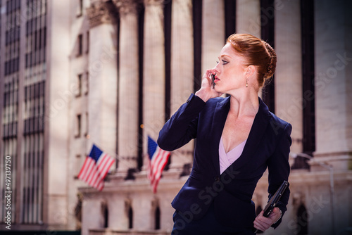 Young American businesswoman working in New York City. Young Woman dressing in blue suit, holding small tablet computer, standing by old office building, looking away, talking on cell phone. .