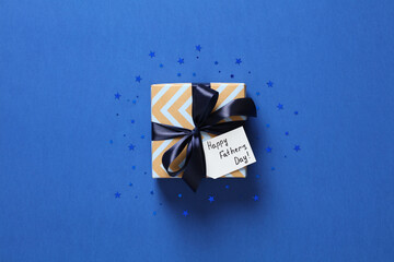 Vintage gift box with blue ribbon bow and label Happy Fathers Day on blue background. Fathers Day present.