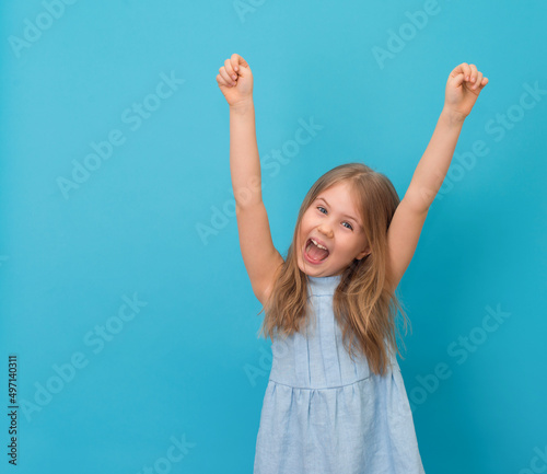 Little excited girl with hands up screeming on blue background.