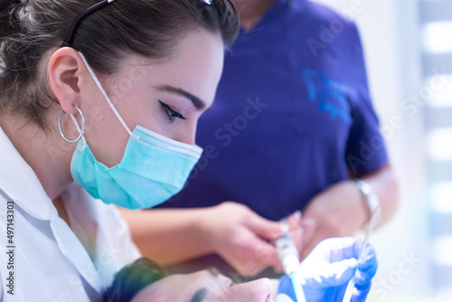 Female dentist in mask holding dental instruments while working with patient in dental clinic