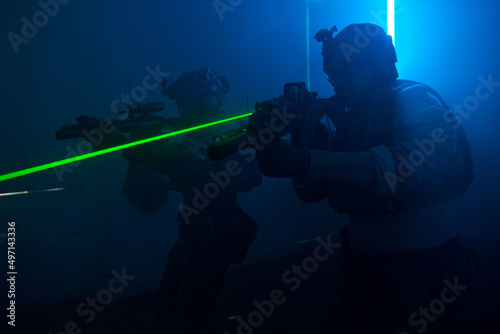 Concentrated men playing strikeball in dark room. Men in military uniforms aiming, looking for enemies. Army, military, game, hobby concept