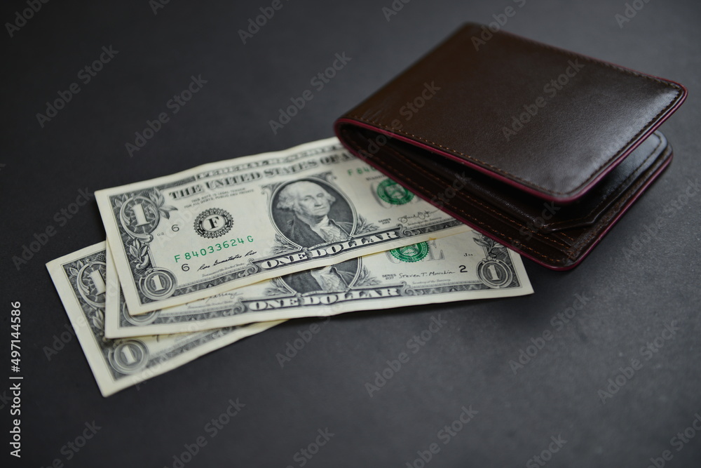 Few one-dollar bills under a men's leather wallet presenting inflation, a lower wage rate, a currency war concept, global economic crisis situation. Shallow depth of field. Selective focus. Few one-dollar bills under a men's leather wallet presenting inflation, a lower wage rate, a currency war concept, global economic crisis situation. Shallow depth of field. Selective focus.