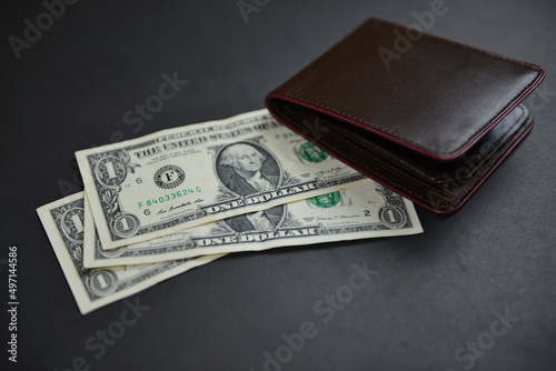 Few one-dollar bills under a men's leather wallet presenting inflation, a lower wage rate, a currency war concept, global economic crisis situation. Shallow depth of field. Selective focus.
