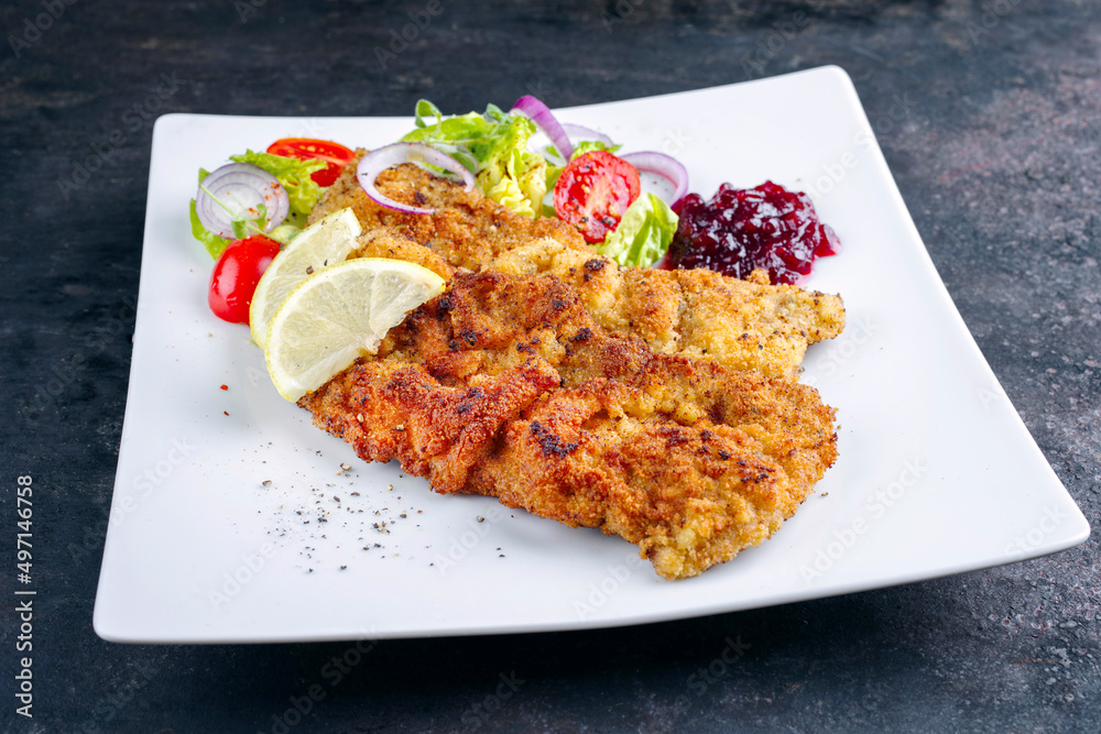 Traditional deep-fried schnitzel with green salad, tomatoes and cranberry jam served as close-up on a design plate Traditional deep-fried schnitzel with green salad, tomatoes and cranberry jam served as close-up on a design plate