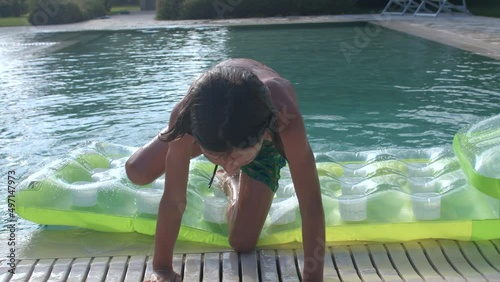 Eight year old child uses green inflatable mattress while swimming in a pool during summer vacations. The ability to swim and the scare of drowning, aquaphobia. Precautions on the water. photo