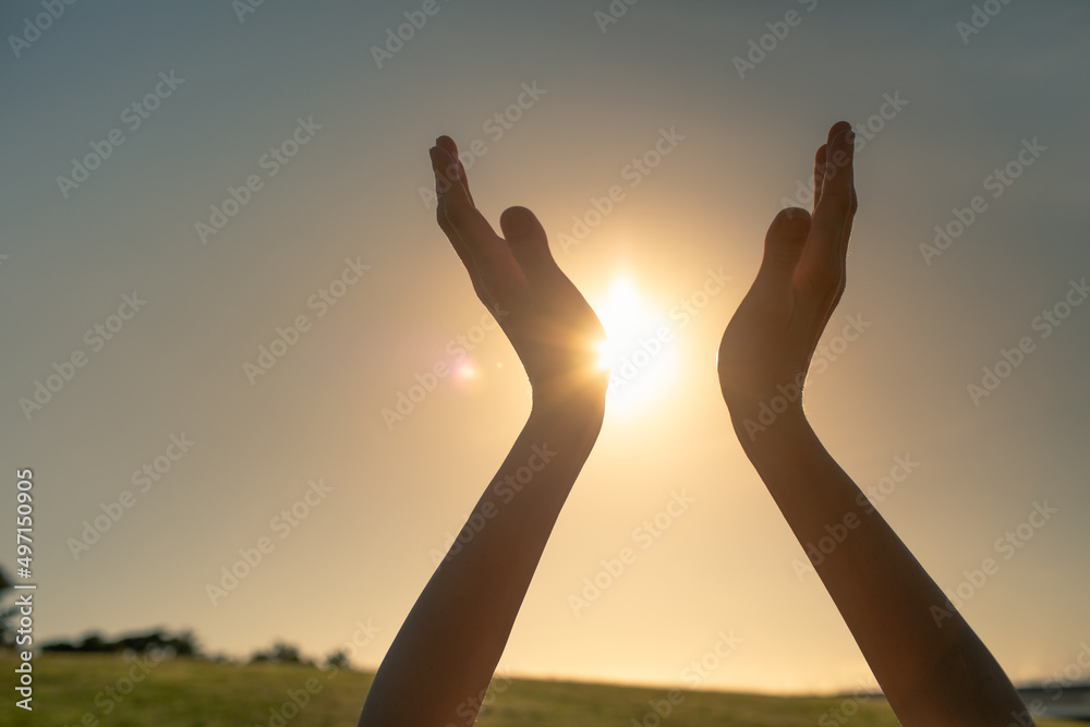Hands reaching out to sky, warm sunshine in the palm of hands. Spiritual healing and light concept 