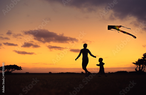Mother and child flying a kite at sunset. Family outdoor fun activity concept. 