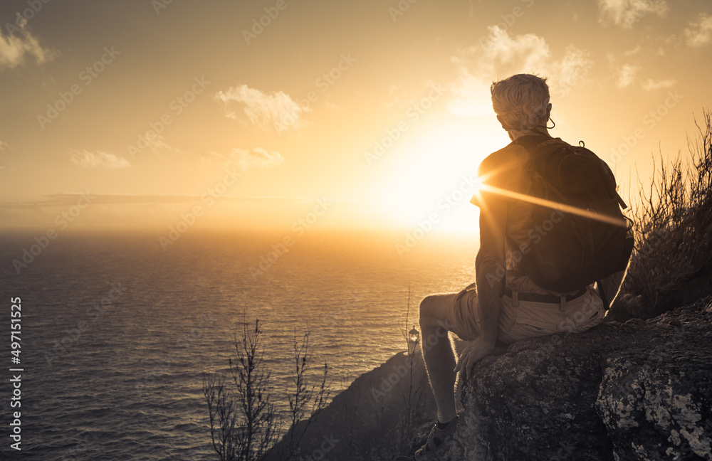 Life is beautiful. Male hiker sitting on a cliff facing a beautiful golden sunrise.	