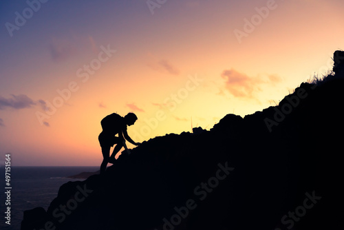 Silhouette of man climbing up a mountain cliff. Goal setting, courage, and will power concept. 