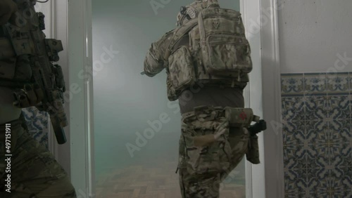 Armed men opening door of ruined building with foot. Handheld shot of focused male participants of airsoft with guns storming building, entering room. Game, teamwork concept