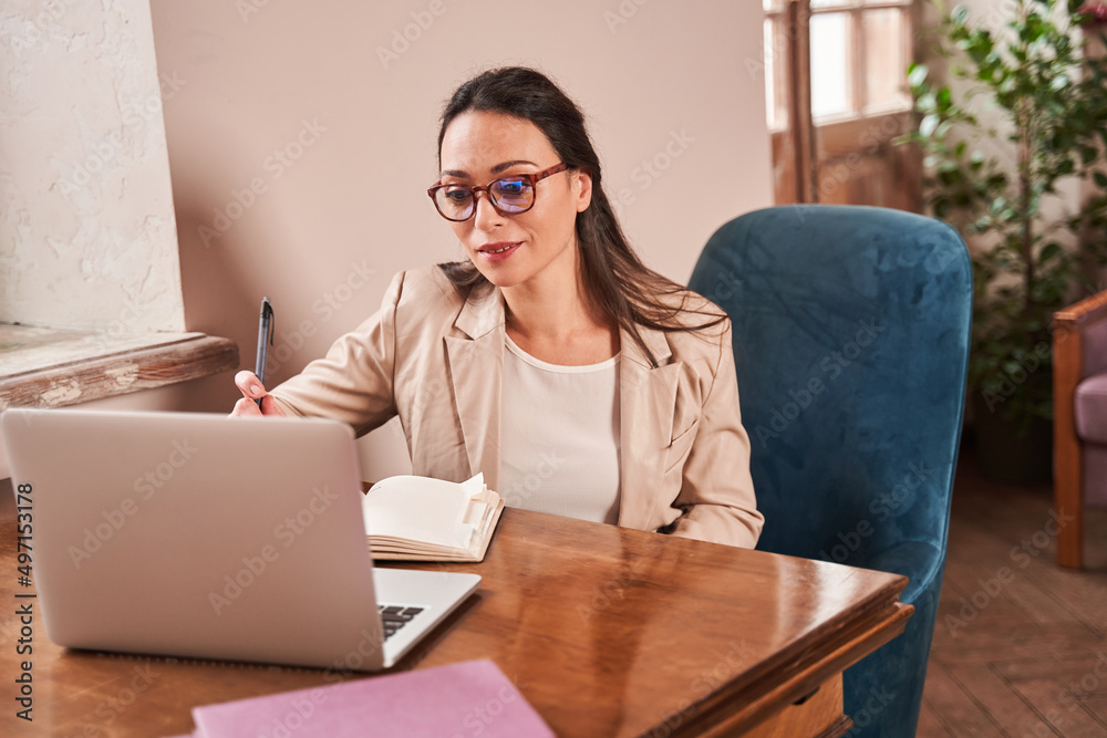 Smiling female therapist watching at her laptop while analysing results of session Smiling female therapist watching at her laptop while analysing results of session