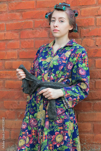 A young beautiful girl stands leaning on a brick wall, she is dressed in a colored flannelette robe, a downy warm scarf is tied around her lower back, her hair is wound in curlers photo