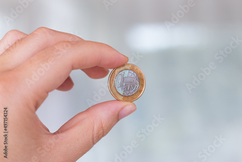 One real coin in the palm of a person's hand. Hand holding a 1 dollar coin. Real is the currency system of the Brazilian Government