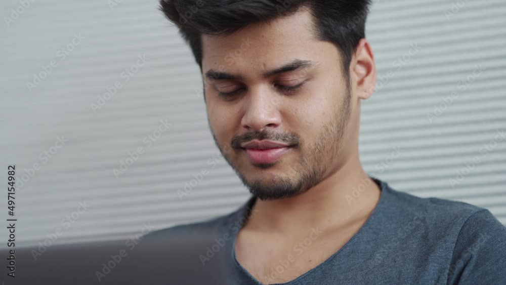 Cheerful Indian man wearing t-shirt working on laptop and correcting his hairstyle at home Cheerful Indian man wearing t-shirt working on laptop and correcting his hairstyle at home