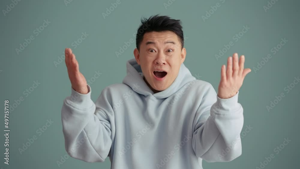 Surprised Asian man wearing hoodie rejoicing at the camera in the blue studio Surprised Asian man wearing hoodie rejoicing at the camera in the blue studio