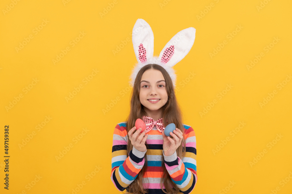 cheerful teen kid in bunny ears and bow tie hold easter eggs on yellow background